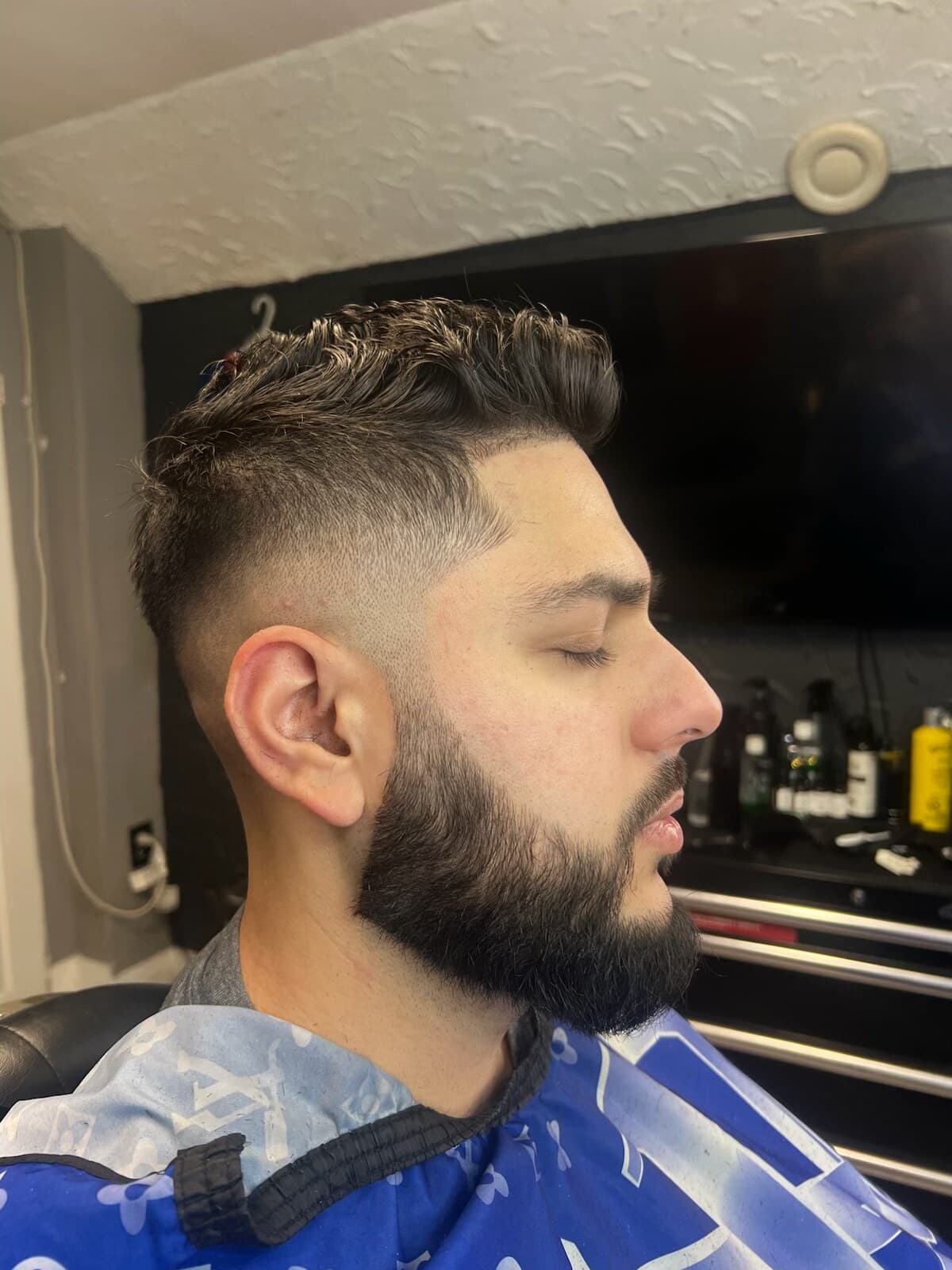 A high skin fade with a textured top and a sculpted full beard, in side profile